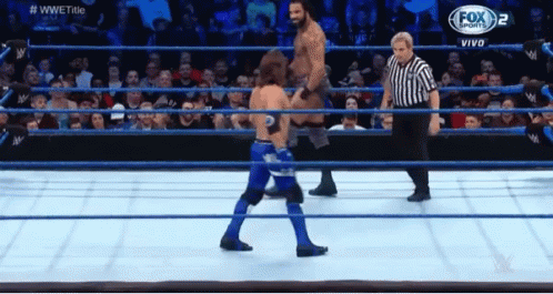 Two Men Are Wrestling In A Wrestling Ring With A Referee In The Background . GIF