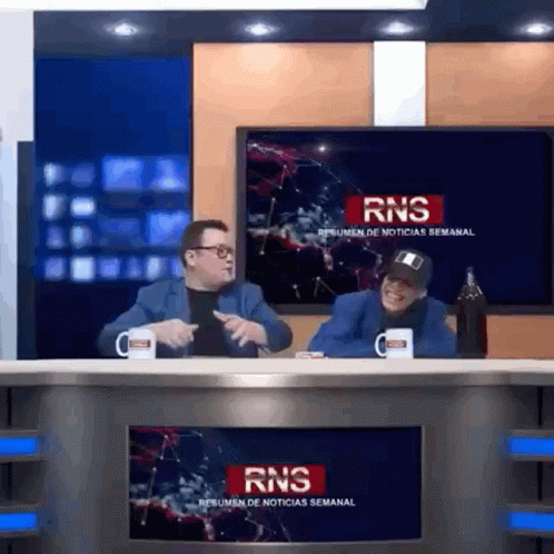 Two Men At Desk In Front Of RNS Resumen De Noticias Semanal Screen GIF