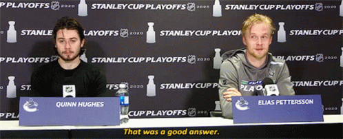Two Men at Table With Quinn Hughes Sign