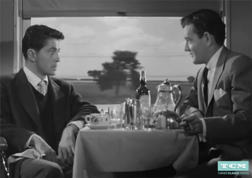 Two Men at Table With Wine Bottle and TCM Logo
