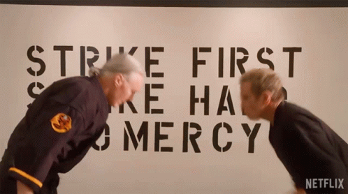 Two Men Bending Over In Front Of Strike First And Mercy Sign GIF