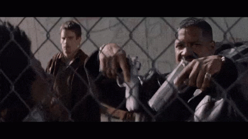 Two Men by Chain Link Fence, One With Gun