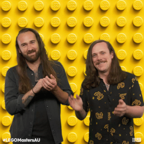 Two Men Clapping on Yellow Background with Lego Bricks