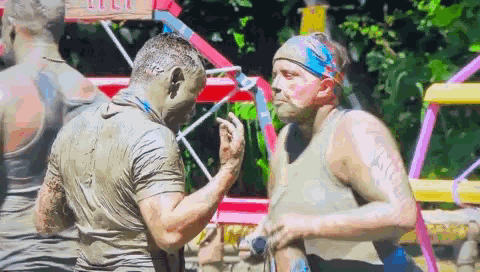 Two Men Covered In Mud Are Standing Next To Each Other In A Muddy Field . GIF