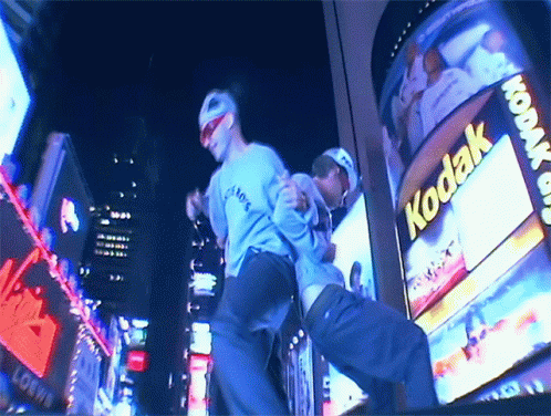 Two Men Dancing in Front of Kodak Billboard