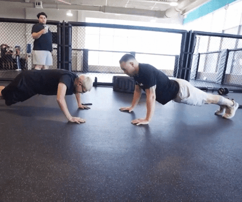 Two Men Do Push Ups In A Gym With A Man Standing Behind Them GIF
