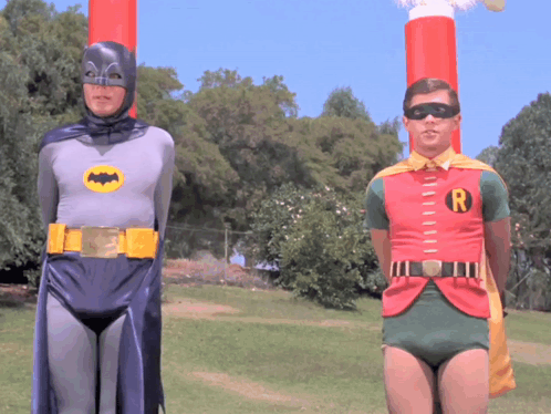 Two Men Dressed As Batman And Robin Are Standing Next To Each Other In A Field GIF