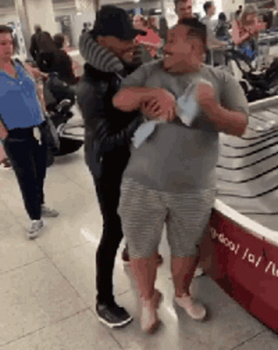 Two Men Hugging at Airport Woman Watches