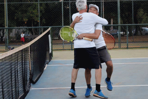 Two Men Hugging Each Other On A Tennis Court With Rackets In Their Hands GIF