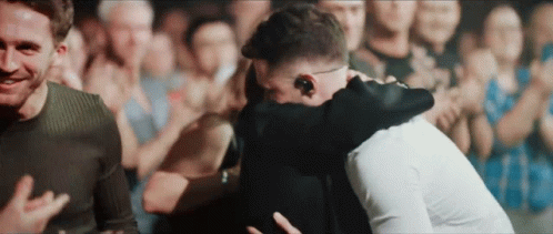 Two Men Hugging In Front Of A Crowd Of People GIF