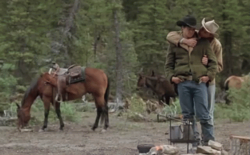 Two Men Hugging In Front Of A Horse In A Field GIF