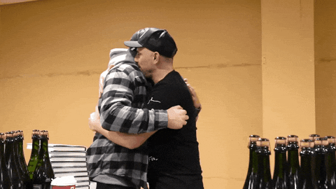 Two Men Hugging In Front Of Bottle Wall GIF