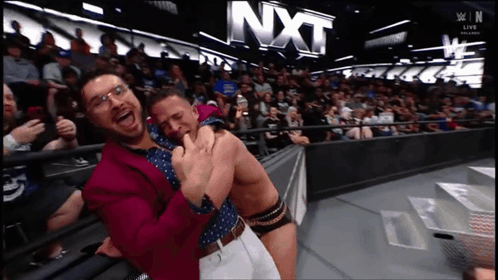 Two Men Hugging In Front Of NXT Sign GIF