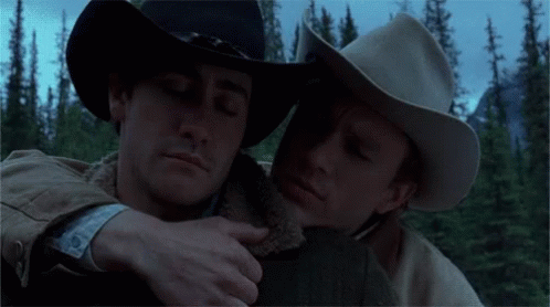 Two Men In Cowboy Hats Hugging Each Other In A Forest GIF