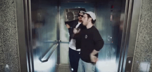 Two Men In Elevator One Wearing Hat And Sunglasses GIF