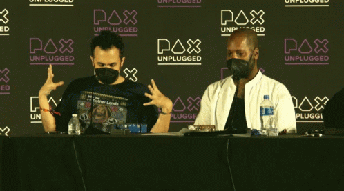 Two Men in Face Masks Sitting in Front of Pax Unplugged Sign