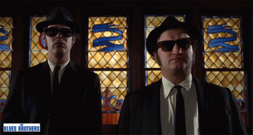 Two Men in Front of Stained Glass Window With Words The Blues Brothers