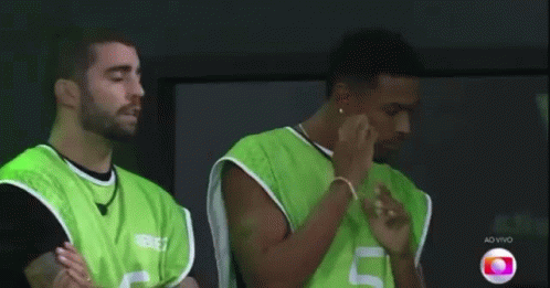 Two Men In Green Vests Are Standing Next To Each Other With Their Arms Crossed . GIF