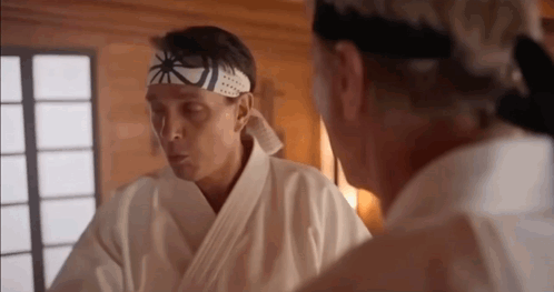 Two Men In Karate Uniforms Are Standing Next To Each Other In A Room And Talking . GIF