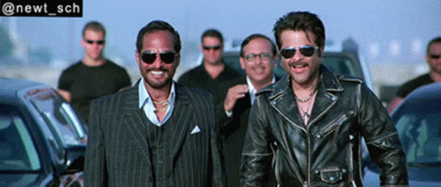 Two Men In Leather Jackets And Sunglasses Smiling Near Cars GIF