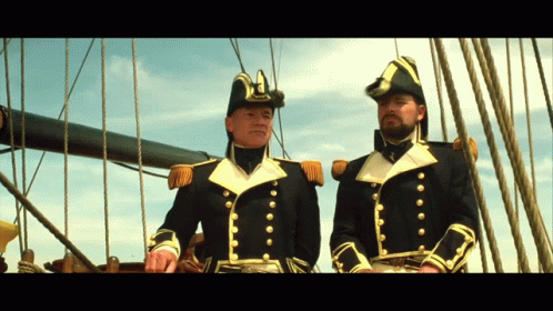 Two Men In Military Uniforms Are Standing On A Boat GIF