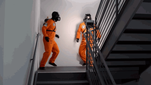 Two Men In Orange Jumpsuits Are Walking Down Stairs GIF