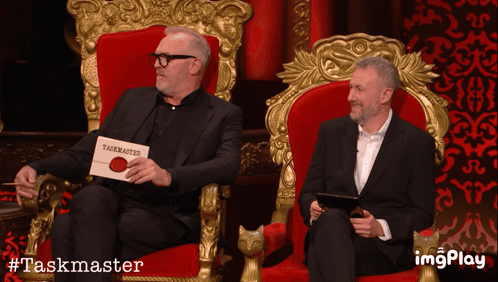 Two Men In Red Chairs With Taskmaster Sign GIF