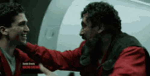 Two Men In Red Jackets Are Hugging Each Other In Front Of A White Wall . GIF