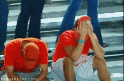 Two Men In Red Shirts Are Sitting On The Ground With Their Hands On Their Faces .. GIF