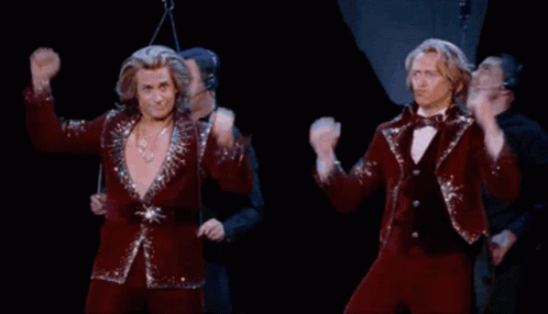 Two Men In Red Suits Are Dancing On A Stage With Their Arms In The Air GIF