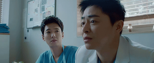 Two Men In Scrubs Are Sitting In A Room And Looking At Something . GIF