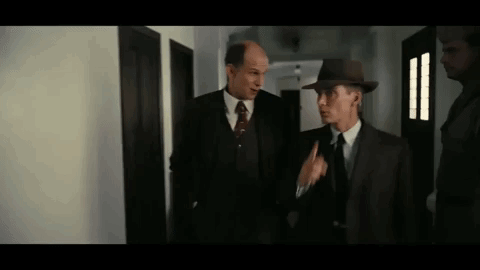 Two Men In Suits And Hats Are Standing Next To Each Other In A Hallway Talking To Each Other . GIF