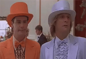 two men in suits and hats are standing next to each other . one of the men is wearing an orange hat .