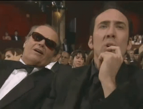 Two Men In Suits And Sunglasses Are Sitting Next To Each Other In A Crowd . GIF