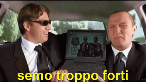 Two Men In Suits And Ties Are Sitting In A Car And One Is Holding A Laptop With A Picture Of A Group Of Men On It GIF