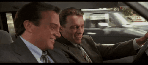 Two Men In Suits And Ties Are Sitting In A Car And One Of Them Is Smiling GIF