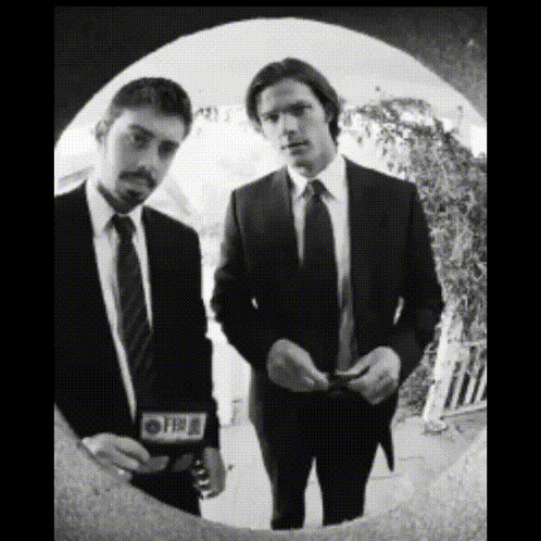 Two Men In Suits And Ties Are Standing Next To Each Other And One Of Them Has A Cbs Sticker On His Jacket GIF