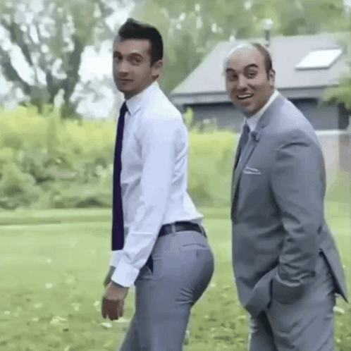 Two Men In Suits And Ties Are Standing Next To Each Other In A Grassy Field . GIF