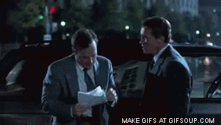 Two Men In Suits And Ties Are Standing Next To Each Other In Front Of A Car And Looking At Papers GIF