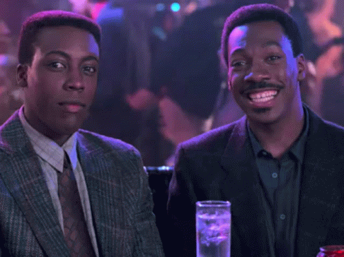 Two Men In Suits And Ties Sitting At Table With Drinks GIF