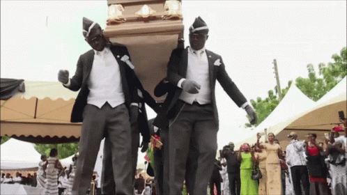 Two Men In Suits Are Carrying A Coffin While Dancing In Front Of A Crowd GIF