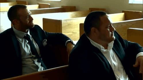 Two Men In Suits Are Sitting In A Church Talking GIF