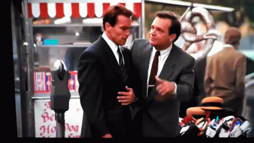 Two Men In Suits Are Standing In Front Of A Hot Dog Cart GIF