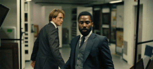 Two Men In Suits Are Walking Down A Hallway And One Has A Beard GIF