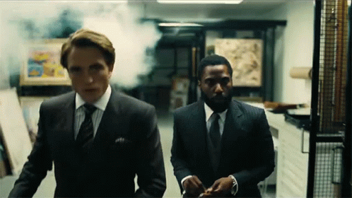 Two Men In Suits Are Walking Down A Hallway With Smoke Coming Out Of It . GIF
