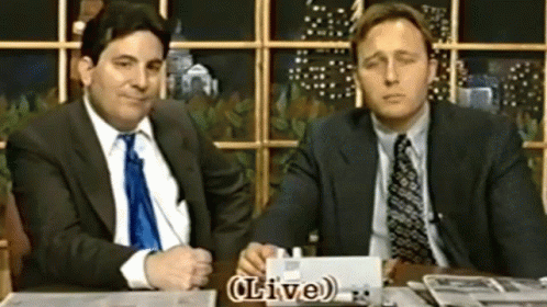 Two Men in Suits at Table With Live Sign