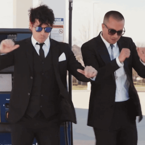 Two Men In Suits Dancing In Front Of A Gas Pump That Says Notice On It GIF