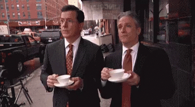 Two Men In Suits Holding Coffee On City Street GIF