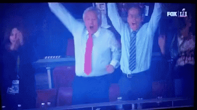 Two Men in Suits Raising Arms in Front of Fox 11 Screen