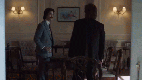 Two Men in Suits Standing in Room with Chairs